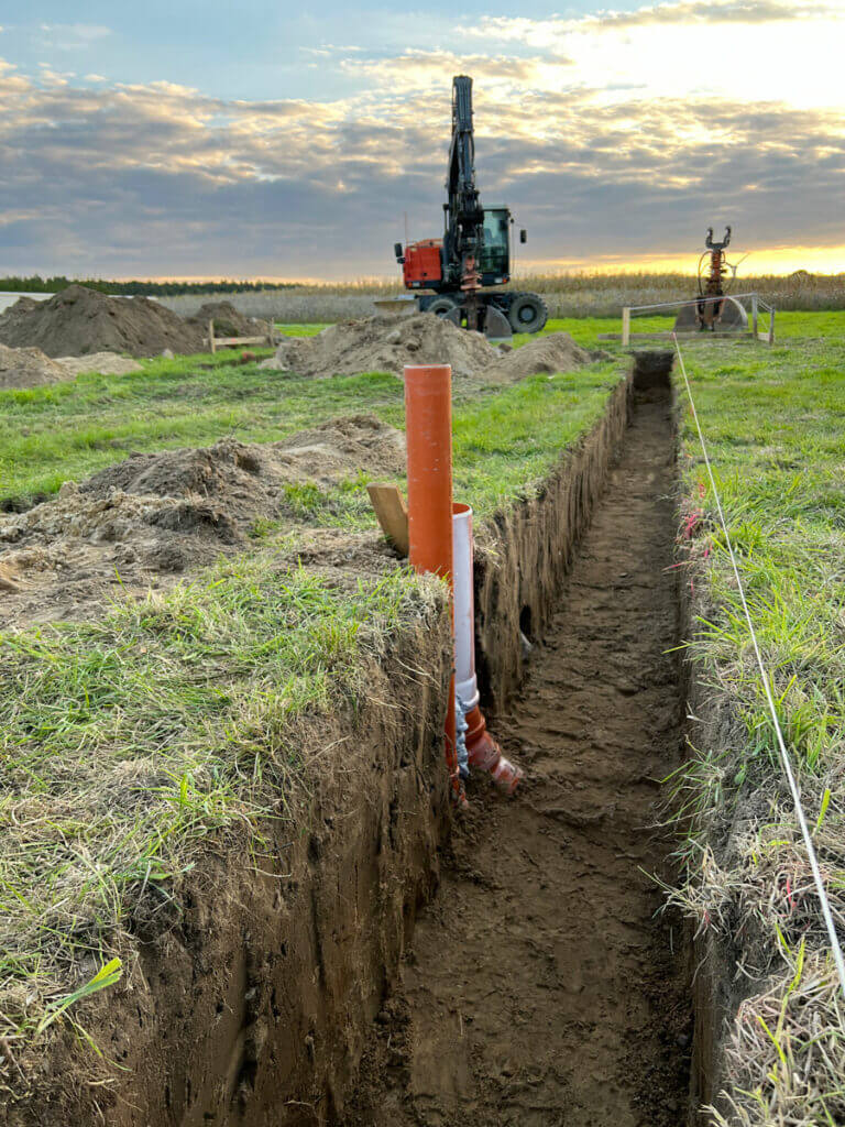 Hauseinführung für die Wärmepumpe. Graben für das Streifenfundament, Radbagger, Grabschaufel und Sonnenuntergang.