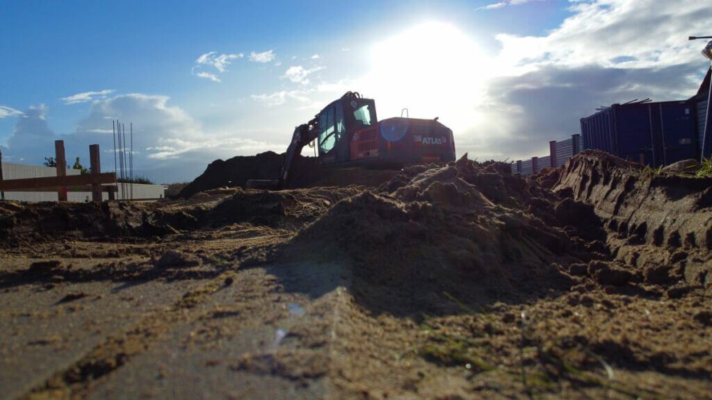 Sauberkeitsschicht am 7. Bautag. Kies, Mineralgemisch, Sonne, Baumaschinen, Dreiecksbock. hier ist einfach alles auf einem Bild.